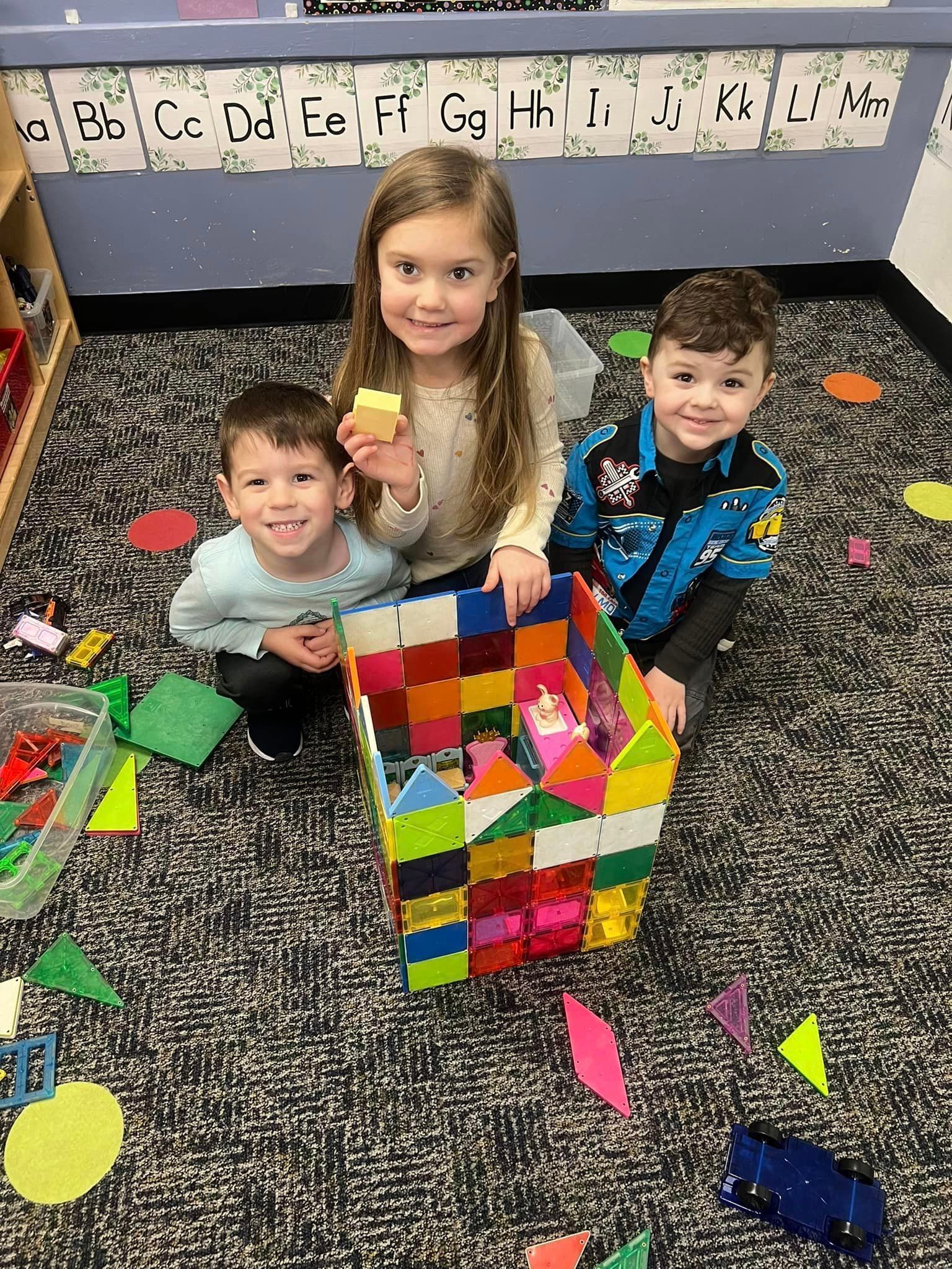 Three children are sitting on the floor playing with blocks.