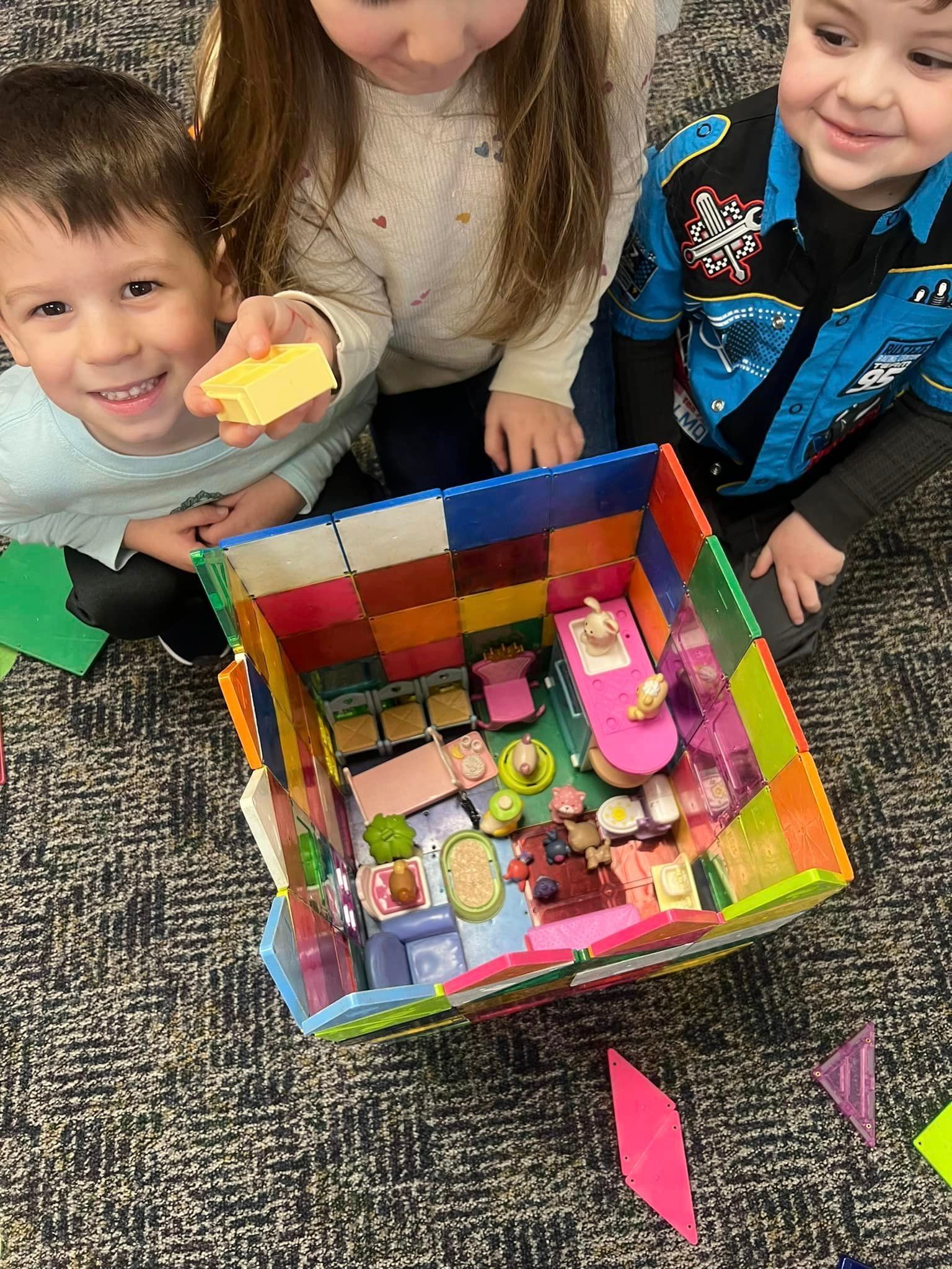 A group of children are sitting on the floor playing with a toy house.