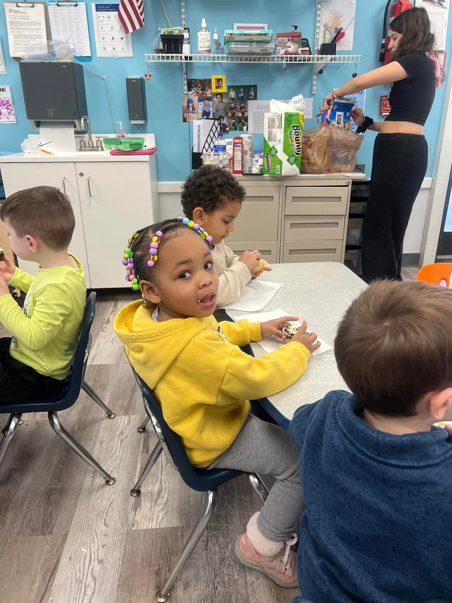 A group of children are sitting at a table in a classroom.