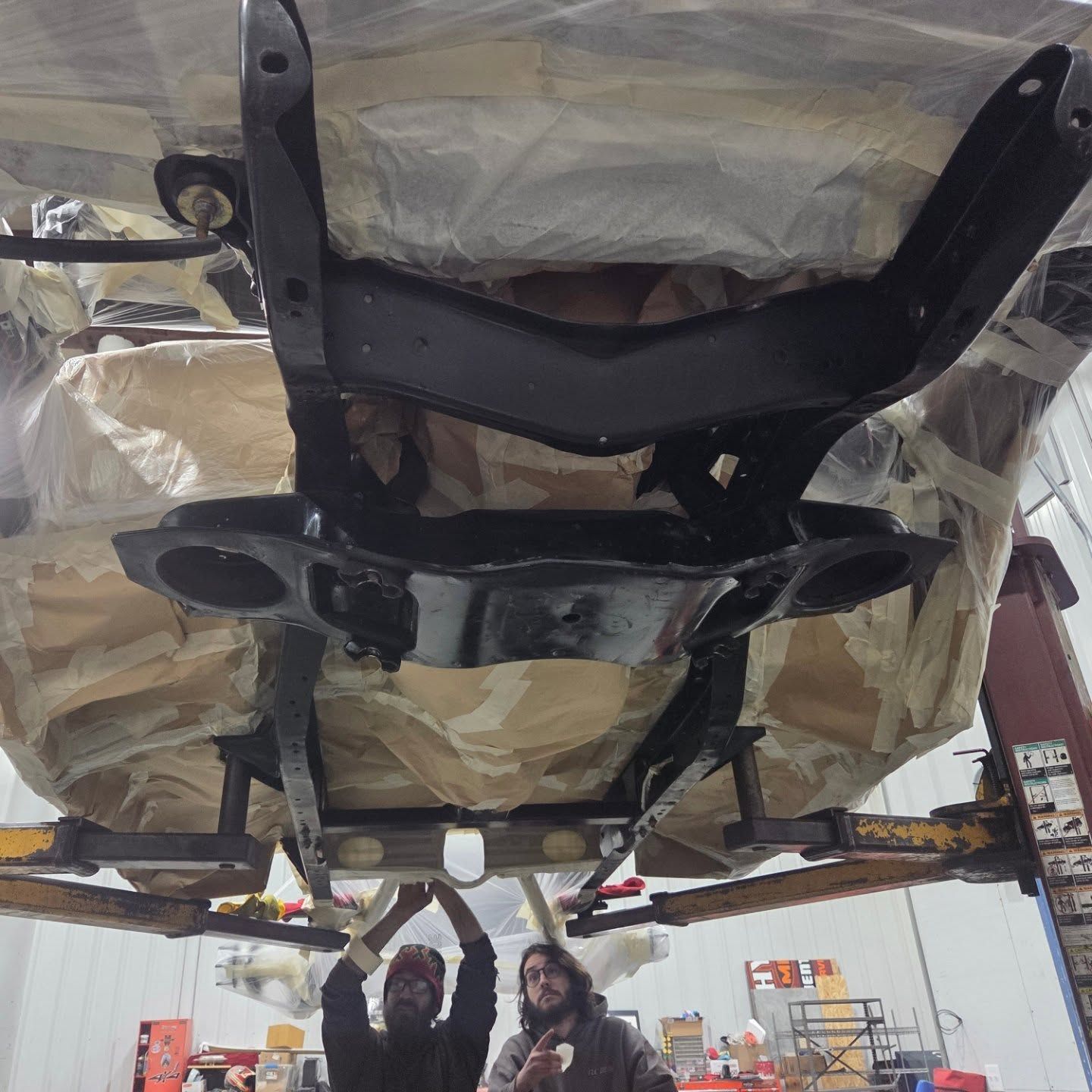 A couple of people standing underneath a car that is being worked on