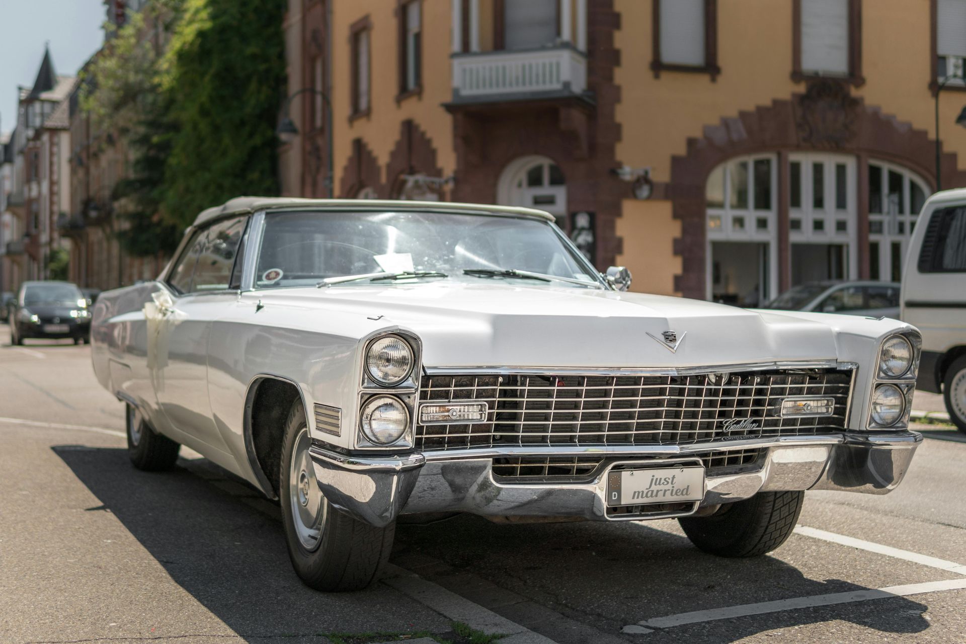 A white cadillac is parked on the side of the road in front of a building.