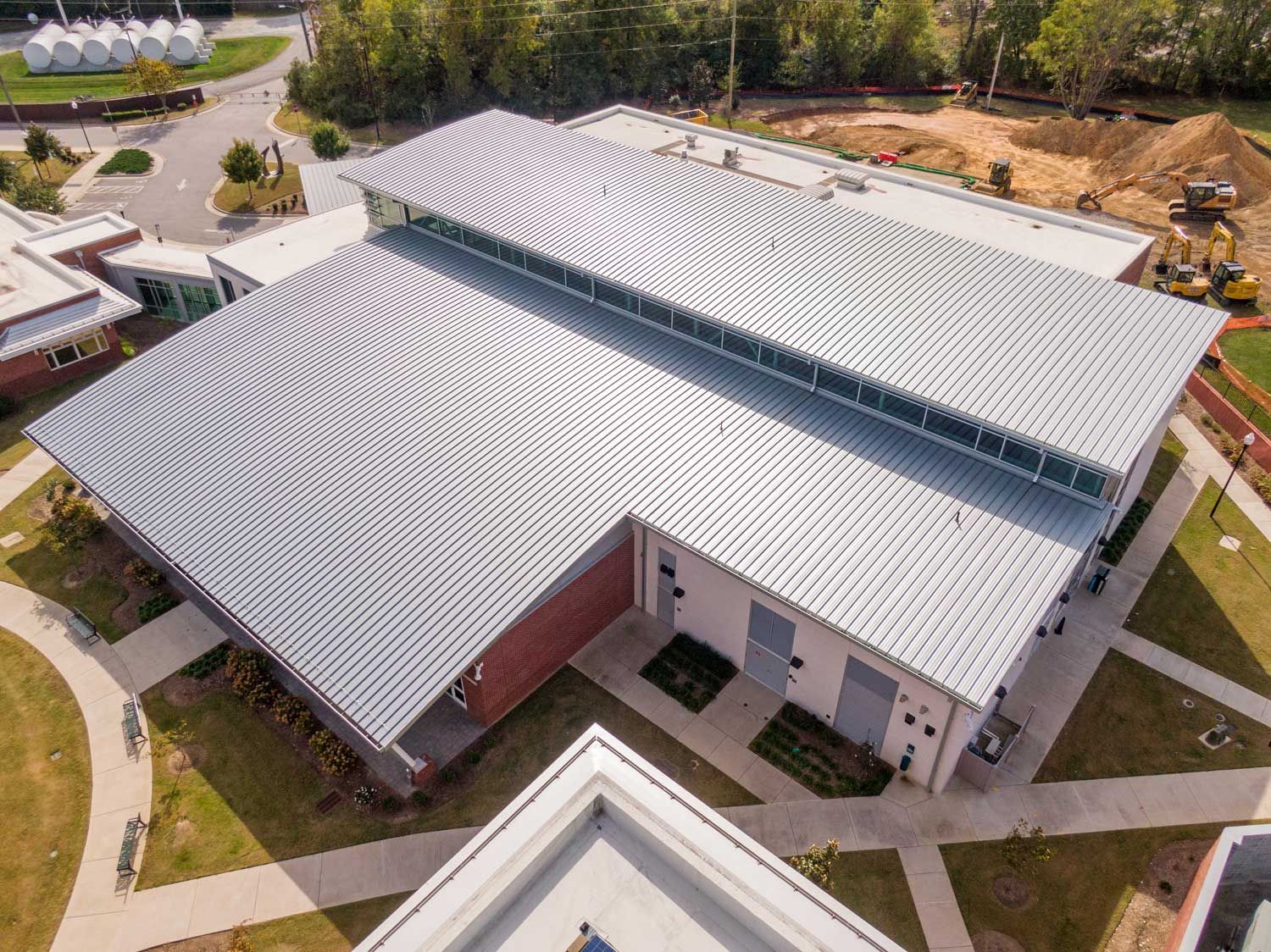 Aerial view of a modern building with a corrugated metal roof. A construction site is visible.