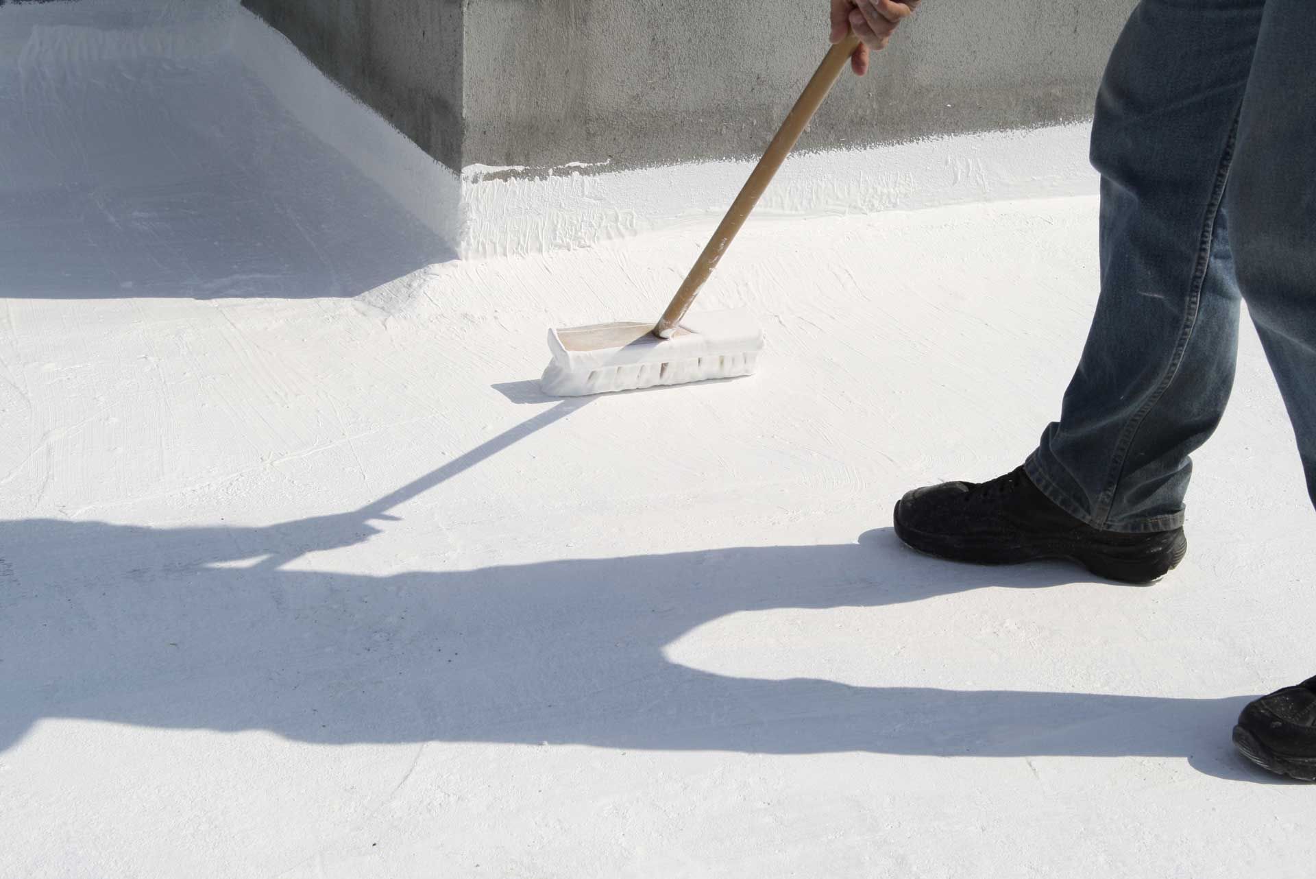 Person applying white coating to a flat roof with a brush.