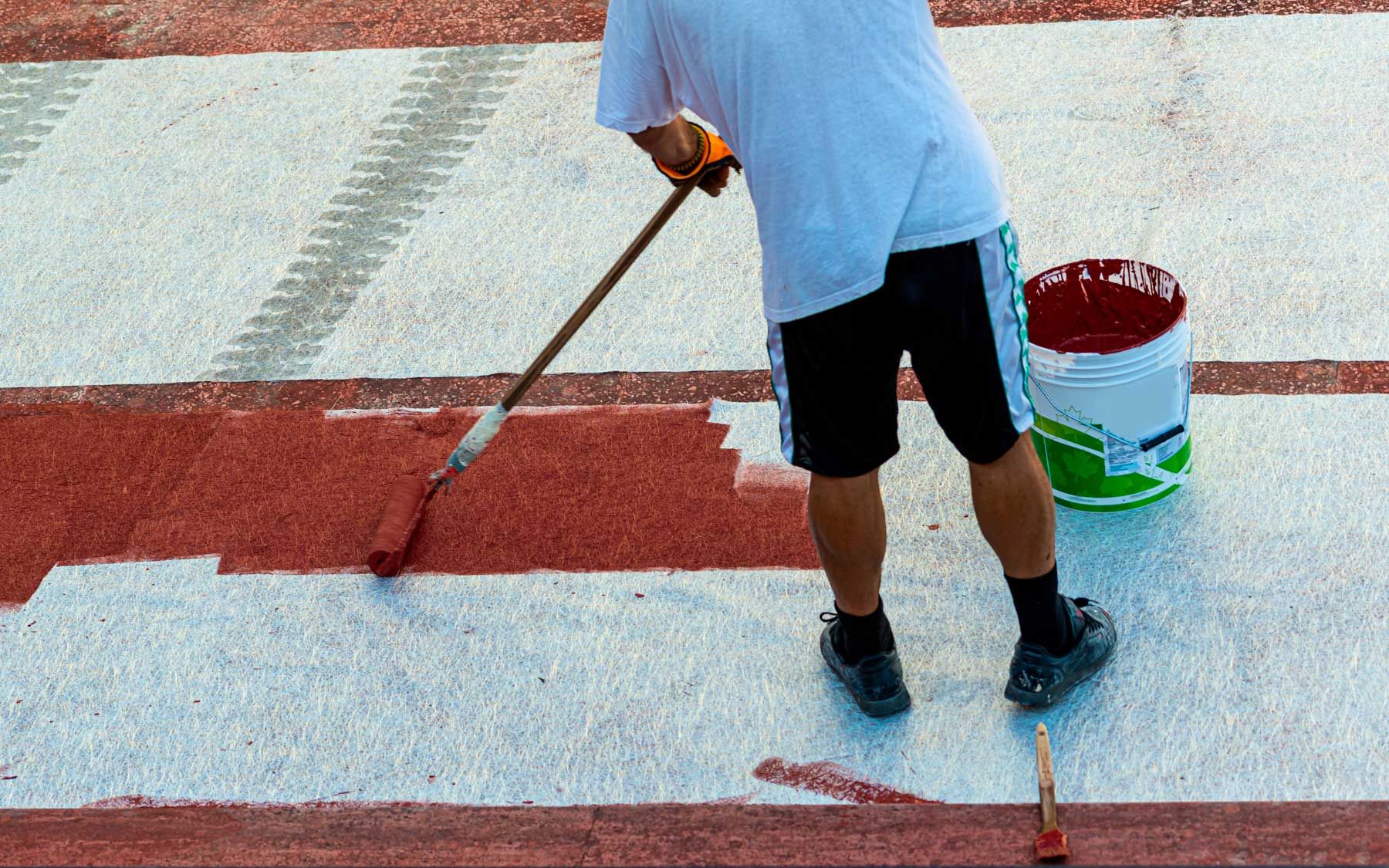 Person paints red line on white surface with a paint roller, bucket of paint nearby. Person paints red line on white surface with a paint roller, bucket of paint nearby.