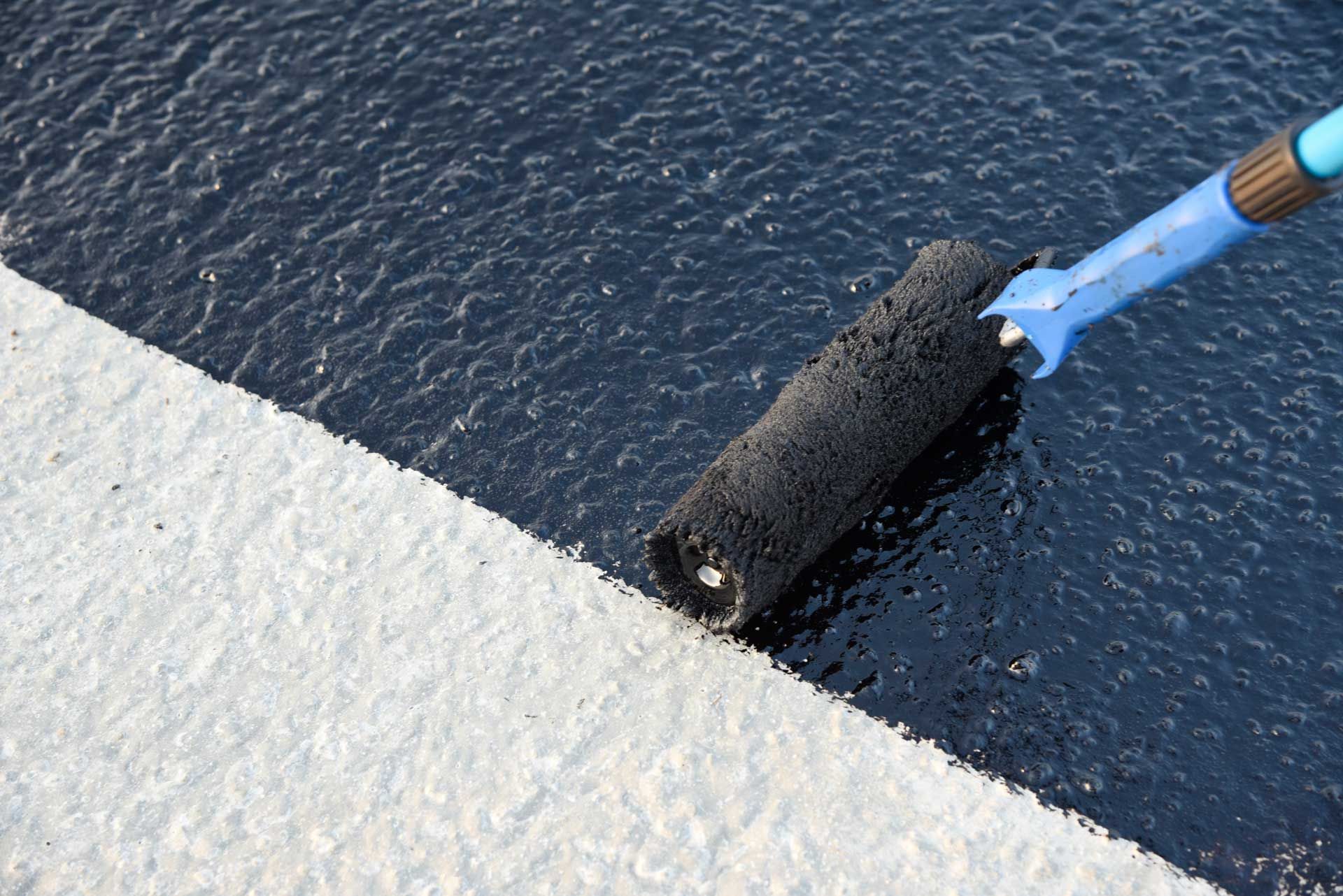Black paint being applied to a concrete surface with a paint roller, creating a contrast. Black paint being applied to a concrete surface with a paint roller, creating a contrast.