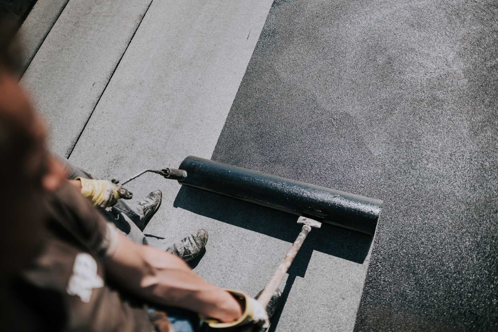 Person applying black sealant to a surface with a roller. Person applying black sealant to a surface with a roller.
