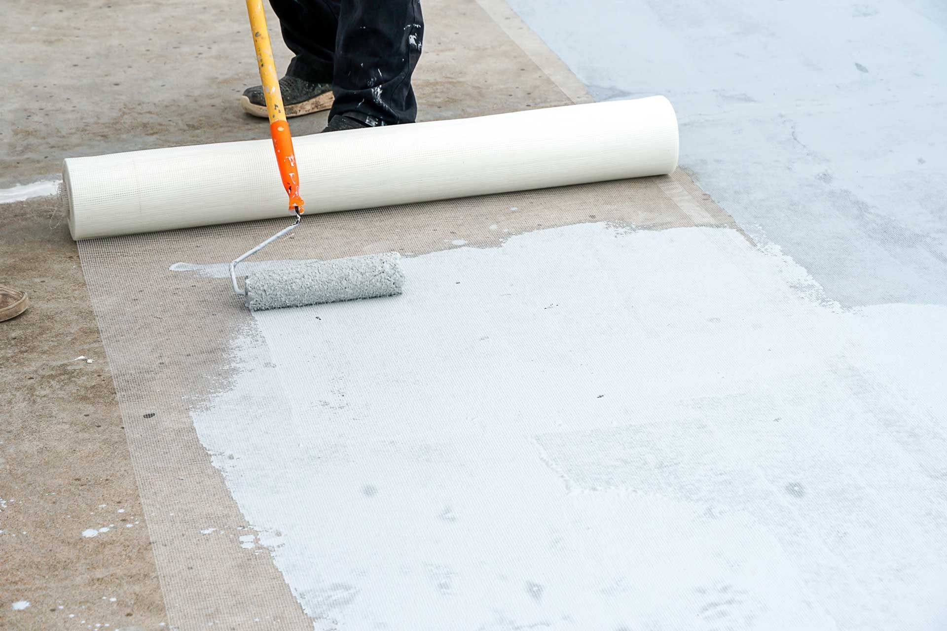 Person applying white coating with roller on a surface, using a large roll.