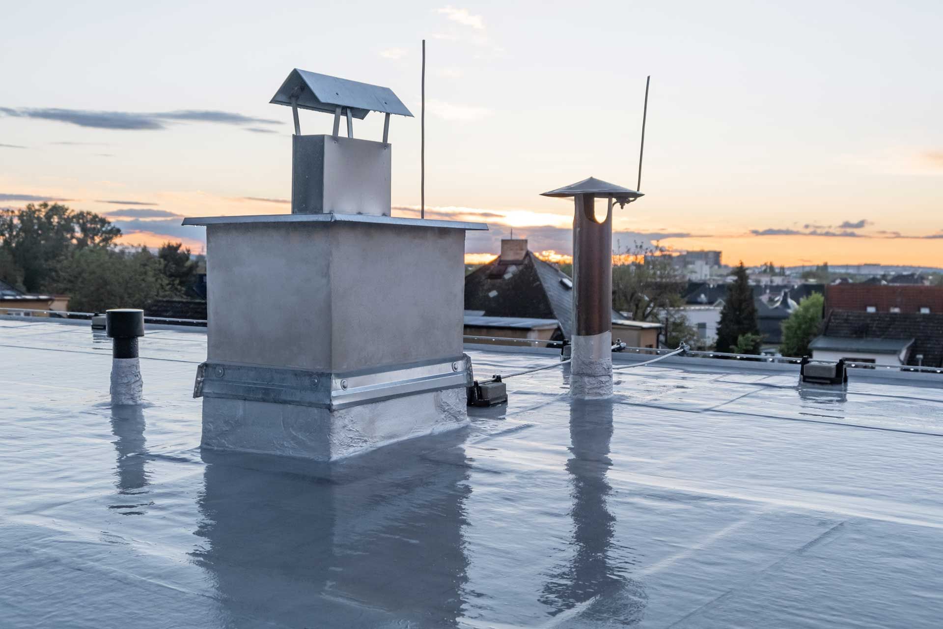 Flat rooftop with chimneys and vents, reflecting a sunset sky.