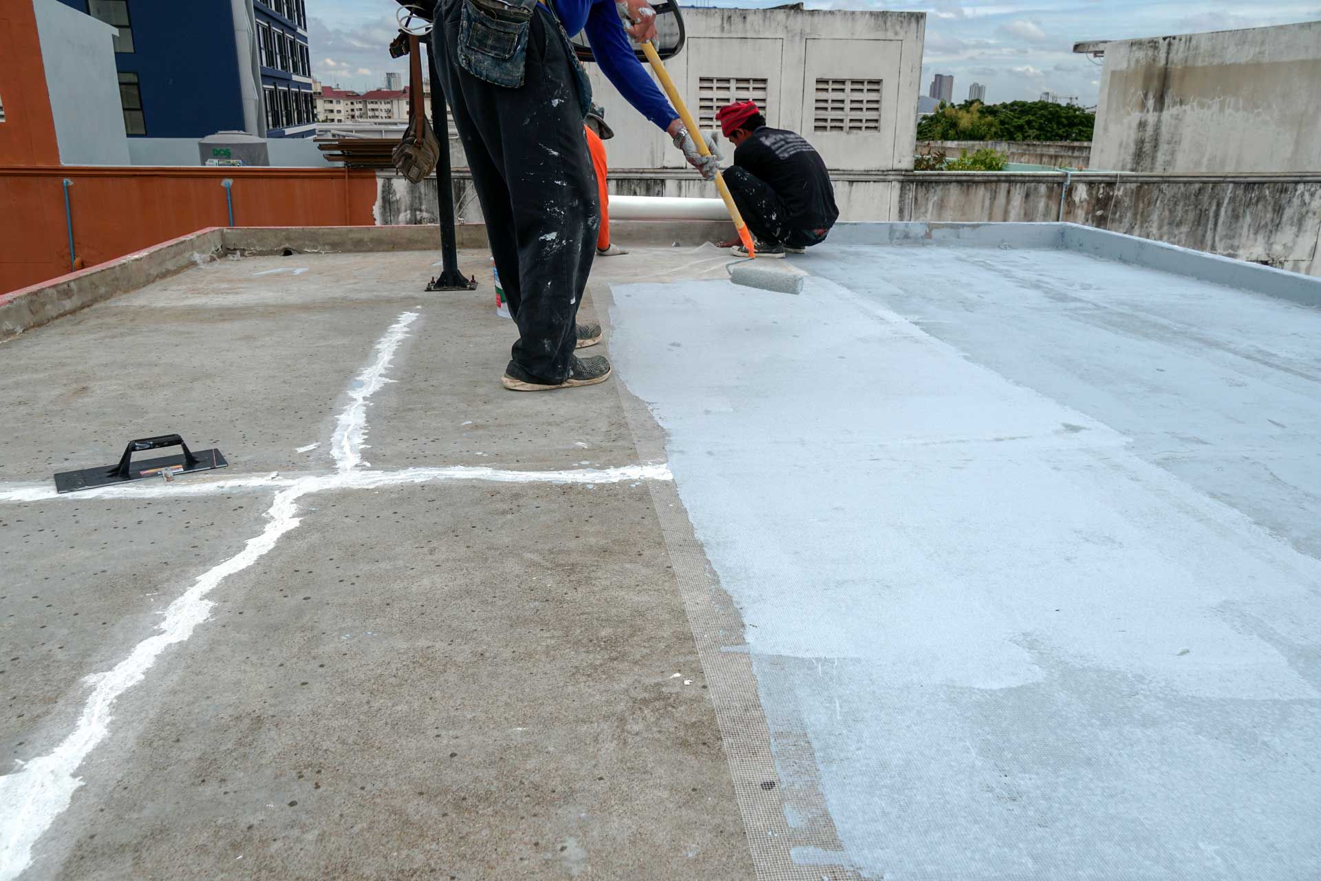 Workers applying gray sealant to a concrete rooftop, with a roller and brush. Workers applying gray sealant to a concrete rooftop, with a roller and brush.