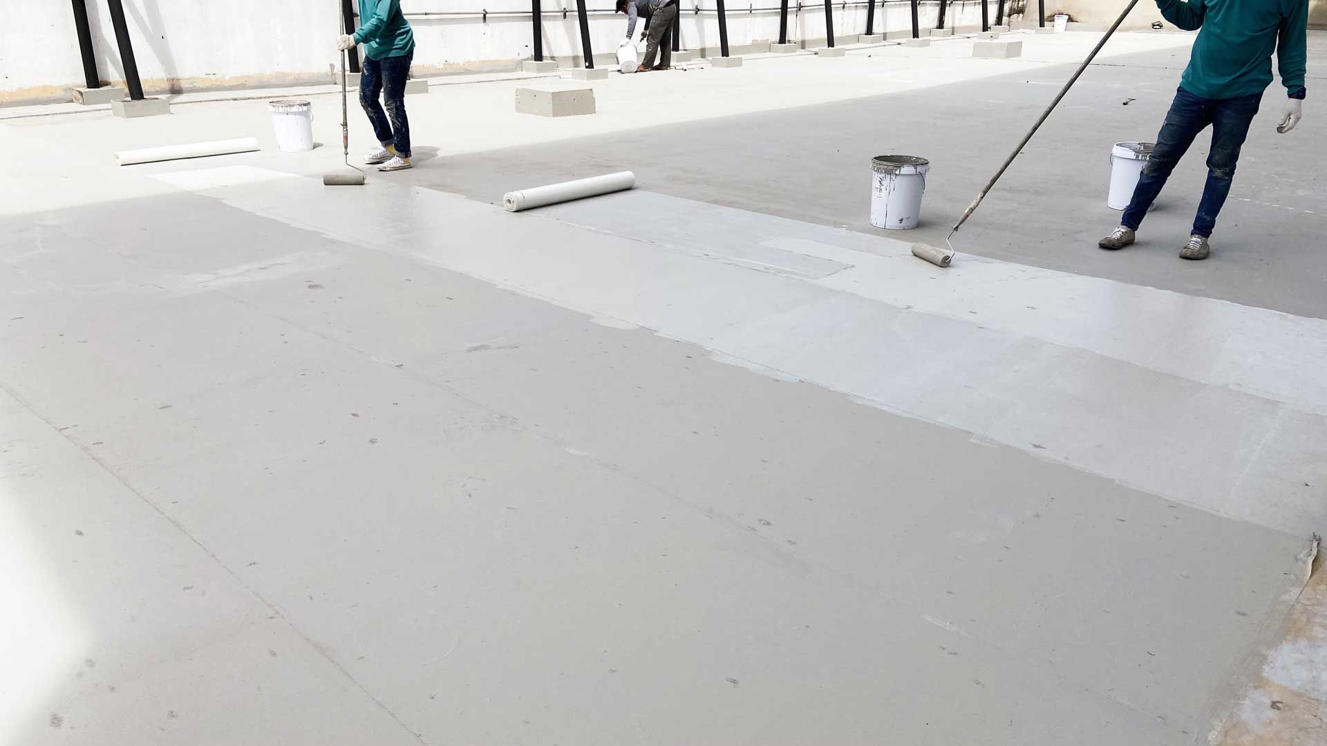 Workers applying a light gray coating to a concrete surface using rollers and buckets. Workers applying a light gray coating to a concrete surface using rollers and buckets.