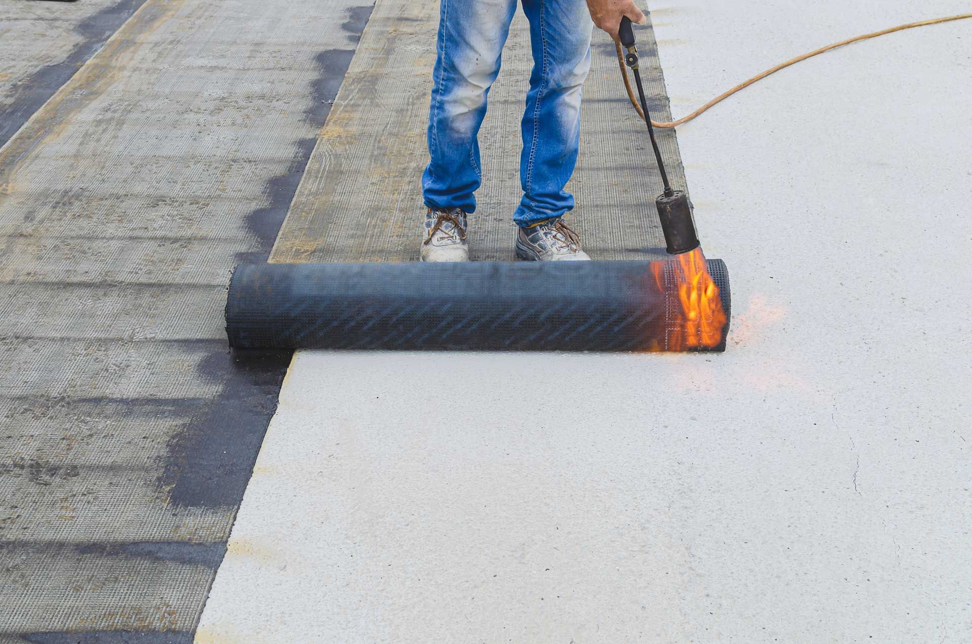 Person using a torch to install roofing material on a white surface.