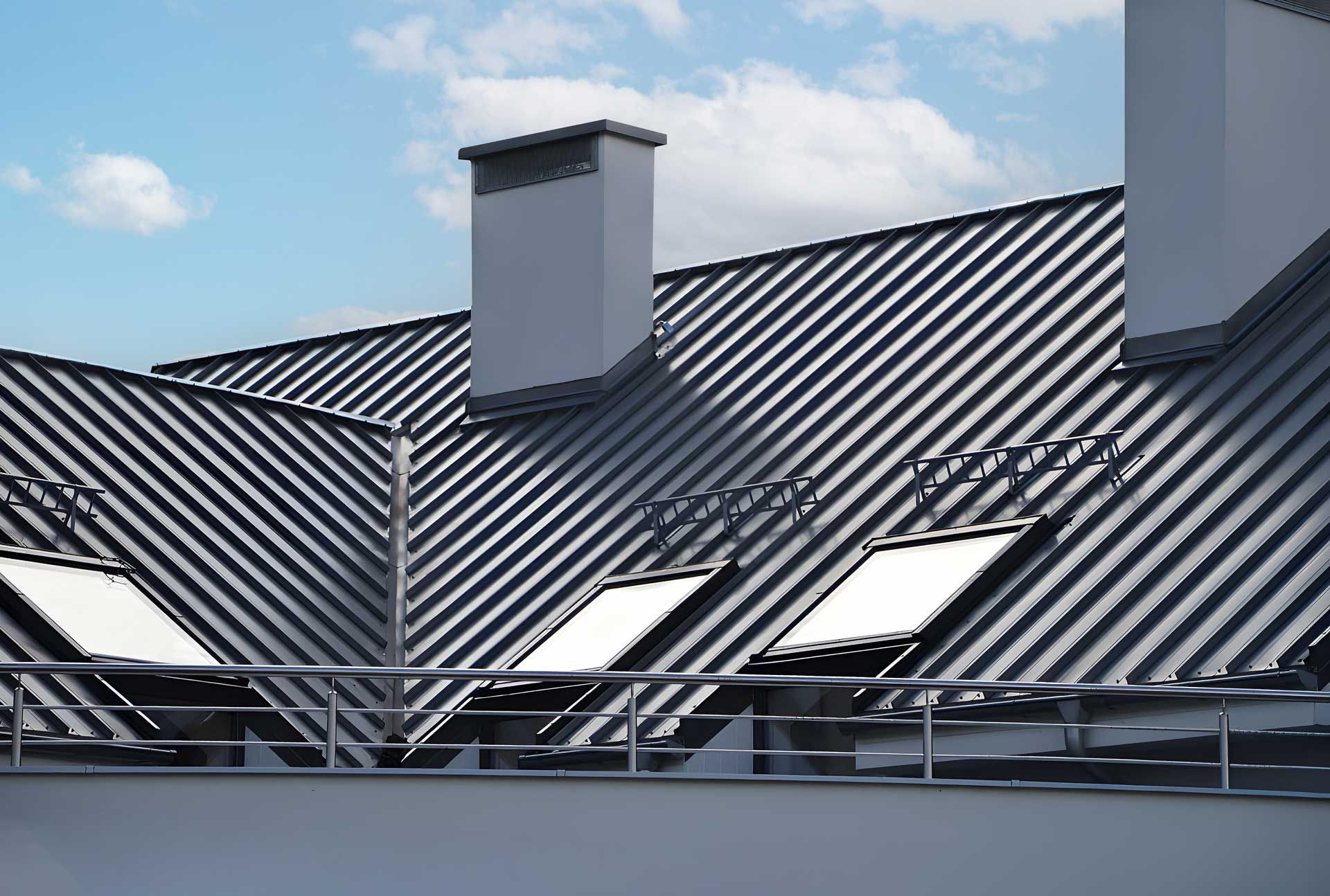 Metal roof with two chimneys and skylights against a partly cloudy sky.