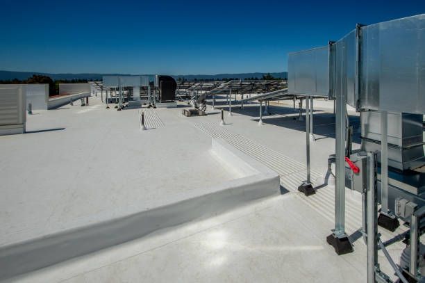 Workers installing roofing material on a flat surface using a torch and roller.