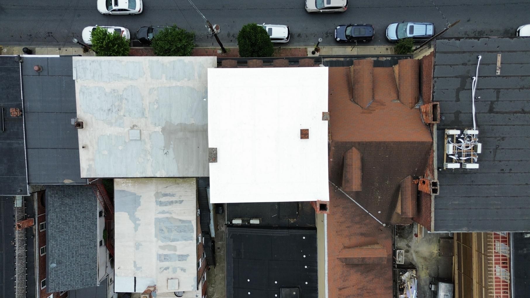 Person paints red line on white surface with a paint roller, bucket of paint nearby.