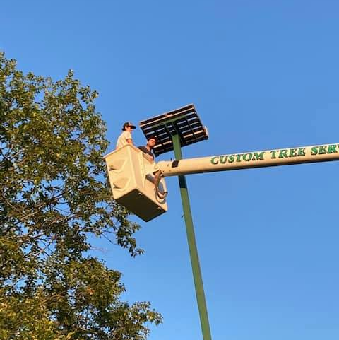 Two people in a bucket truck working on a solar panel, under a clear blue sky.