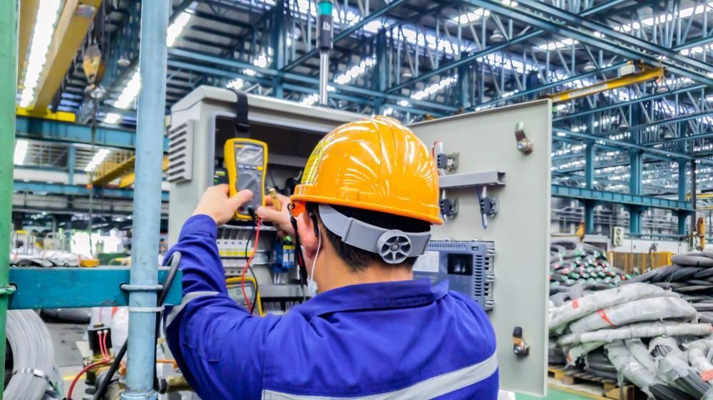 Industrial electrician in safety gear testing electrical control panel inside a factory