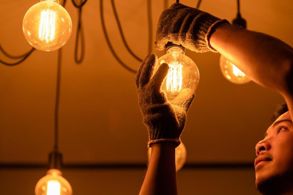 A Man Is Changing a Light Bulb in A Dark Room — Peter Gow Electrical in Lismore, NSW