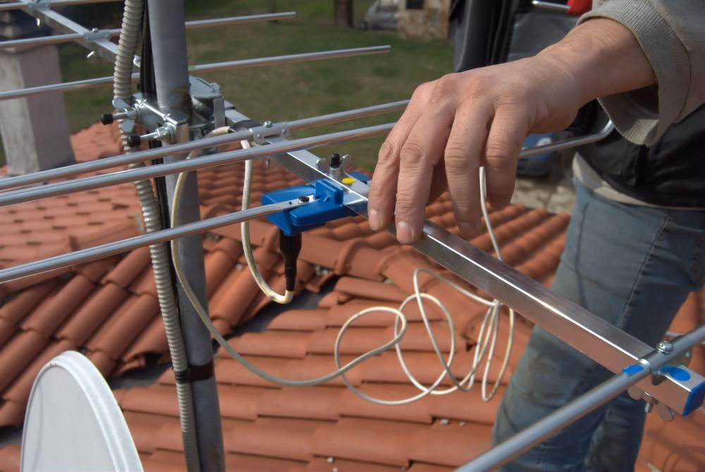 A Man Is Working on An Antenna on A Roof — Peter Gow Electrical in Lismore, NSW
