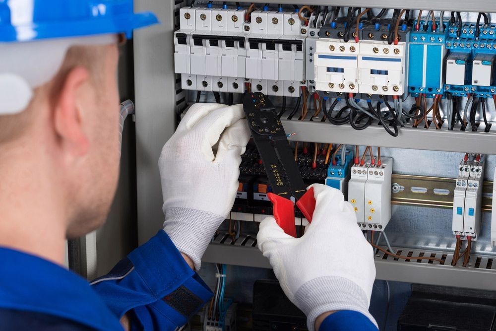 A Man Is Working on An Electrical Panel with A Pair of Pliers — Peter Gow Electrical in Lismore, NSW