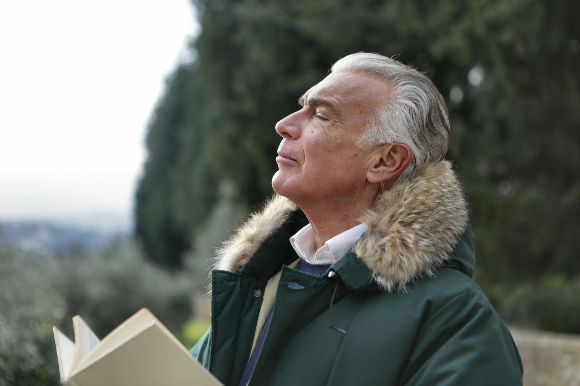 A man in a green jacket is holding a book and looking up.