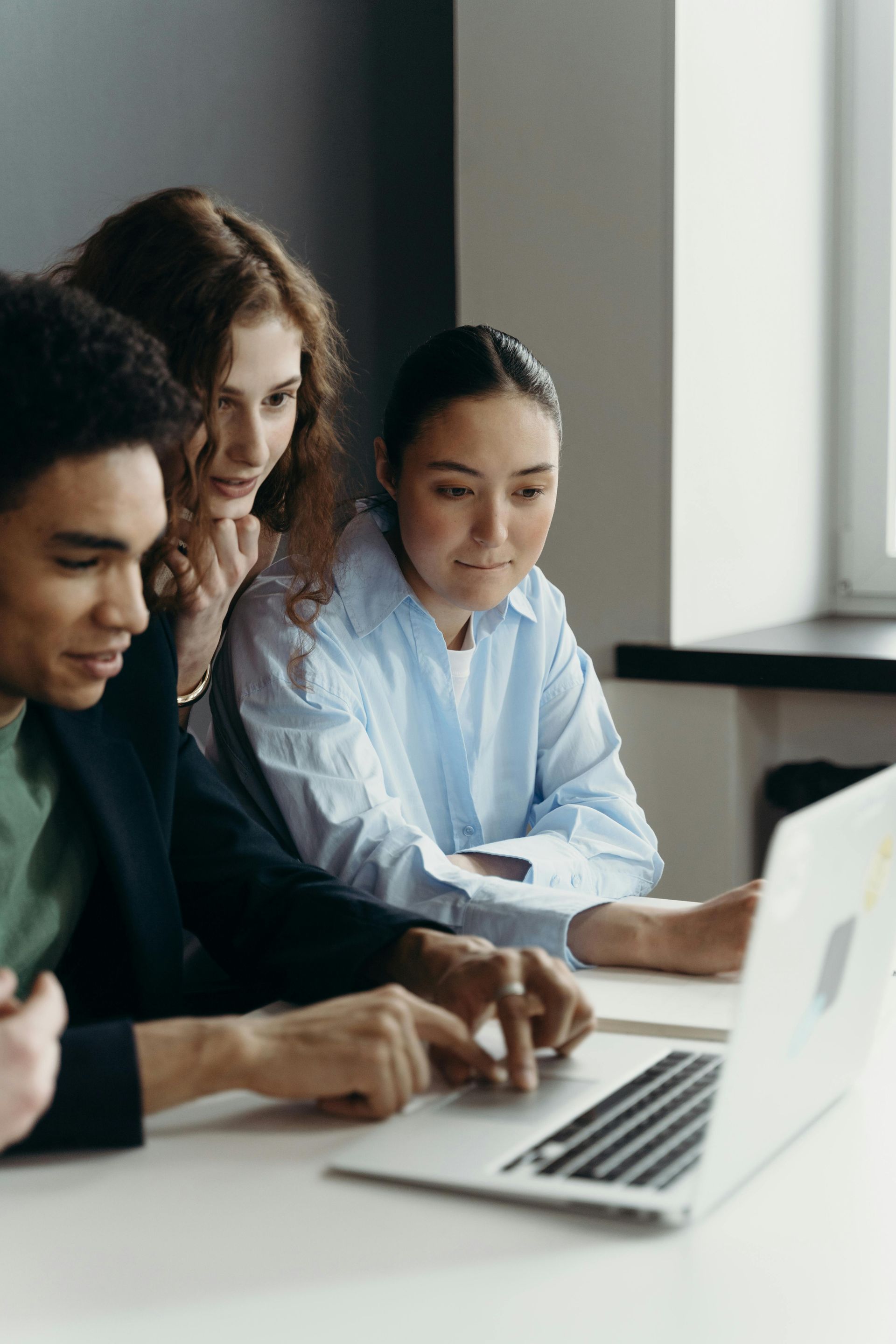 A group of people are sitting at a table looking at a laptop computer.