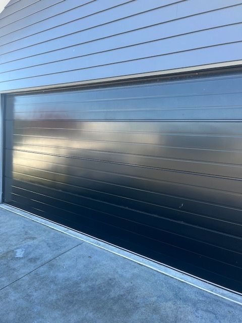 A black garage door is sitting on the side of a building.