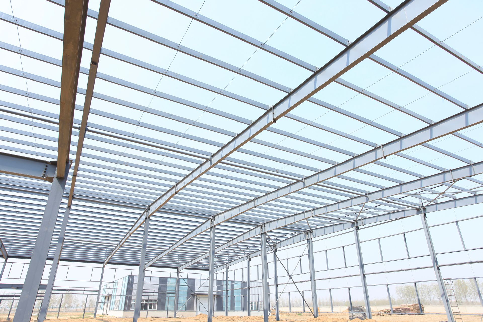 Steel skeleton of a large industrial building under construction against a clear sky.
