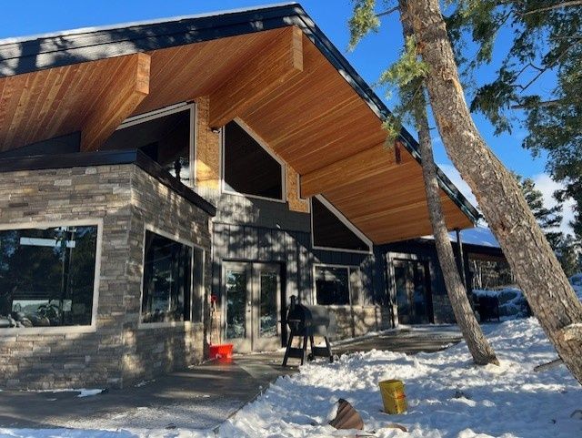 Person on a roof working with a drill, wearing safety gear. Steel support beam visible.
