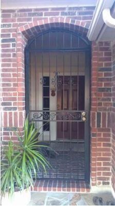 Brick house doorway with black metal security gate and a potted plant beside the entrance