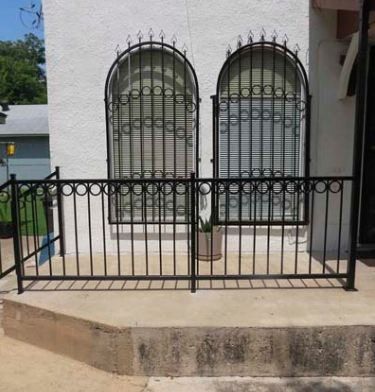 White house facade with two arched windows, black security bars, and a black metal front fence.