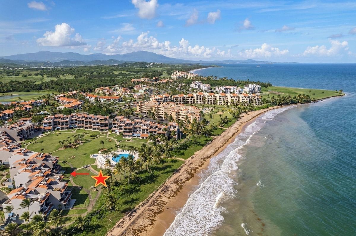 Aerial view of a coastal resort with beach, ocean, buildings, and a pool. A star is placed in front of one of the buildings.