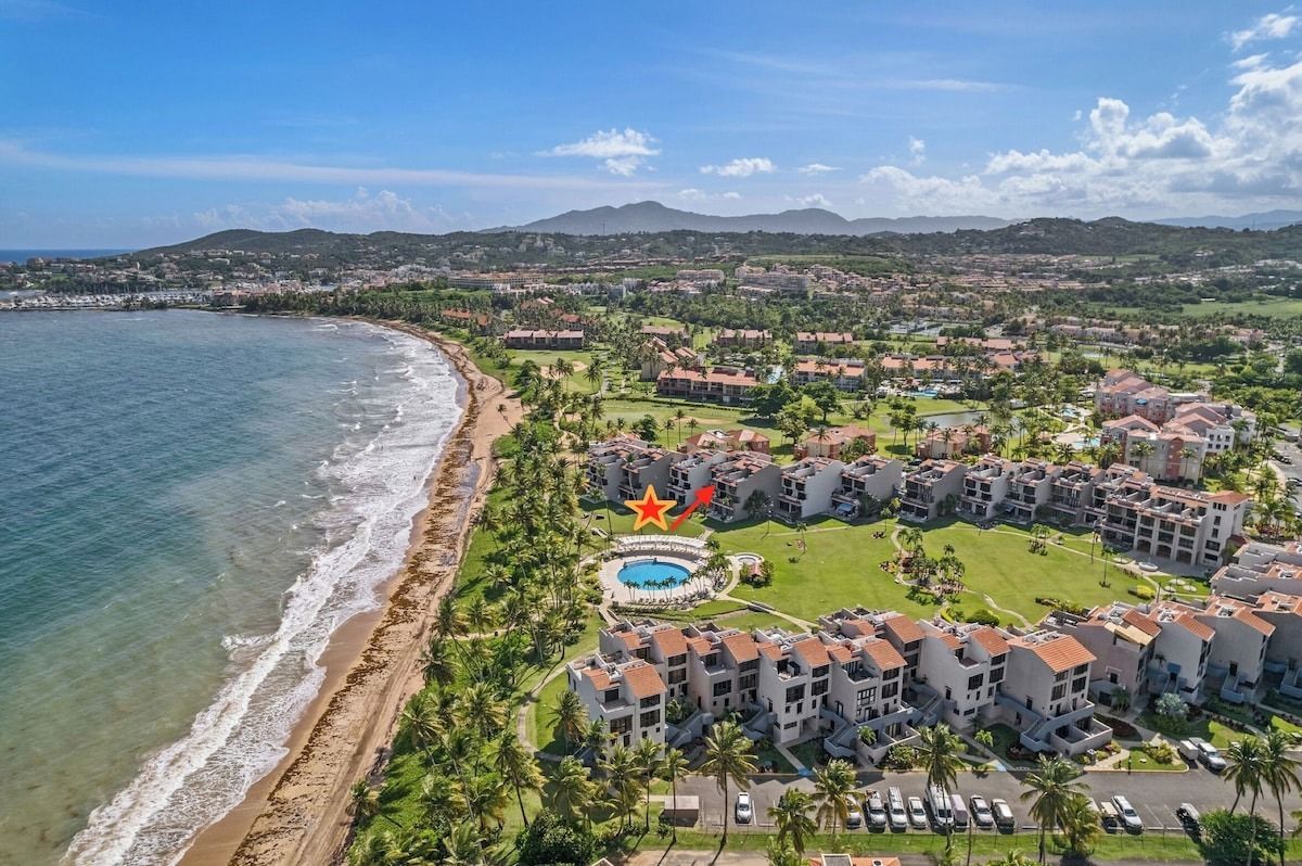 Aerial view of beachfront condos, pool, and coastline under a blue sky.