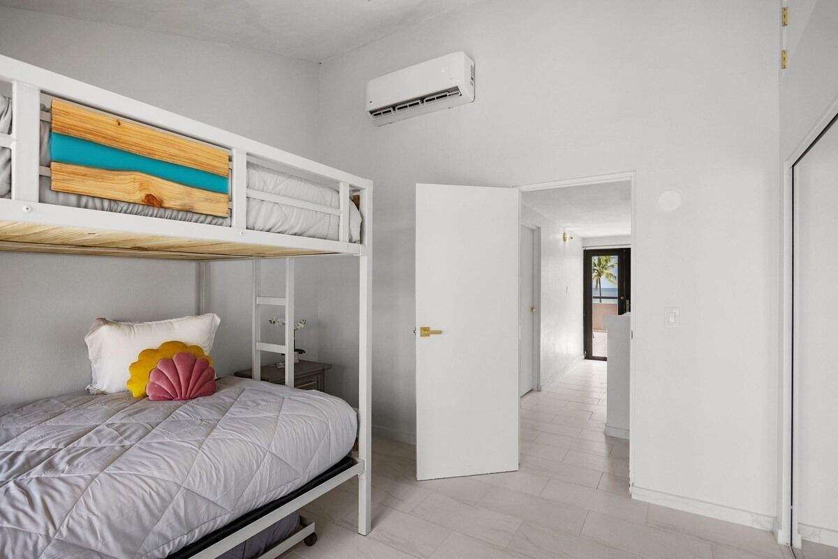 A bunk bed in a bedroom. The upper bunk has a wooden headboard with blue accents. A door leads to a hallway.