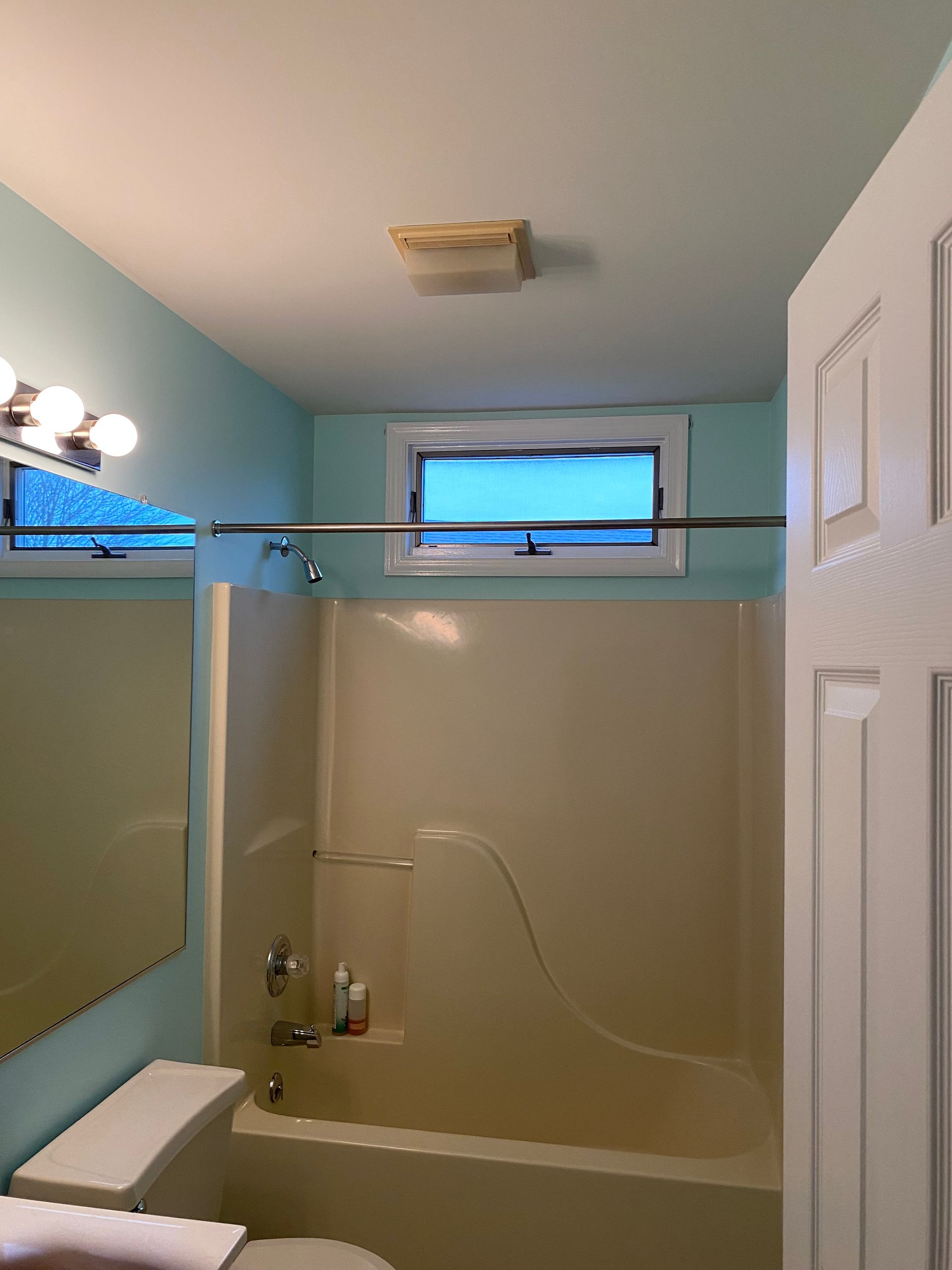 A bathroom with a tub , toilet , mirror and window