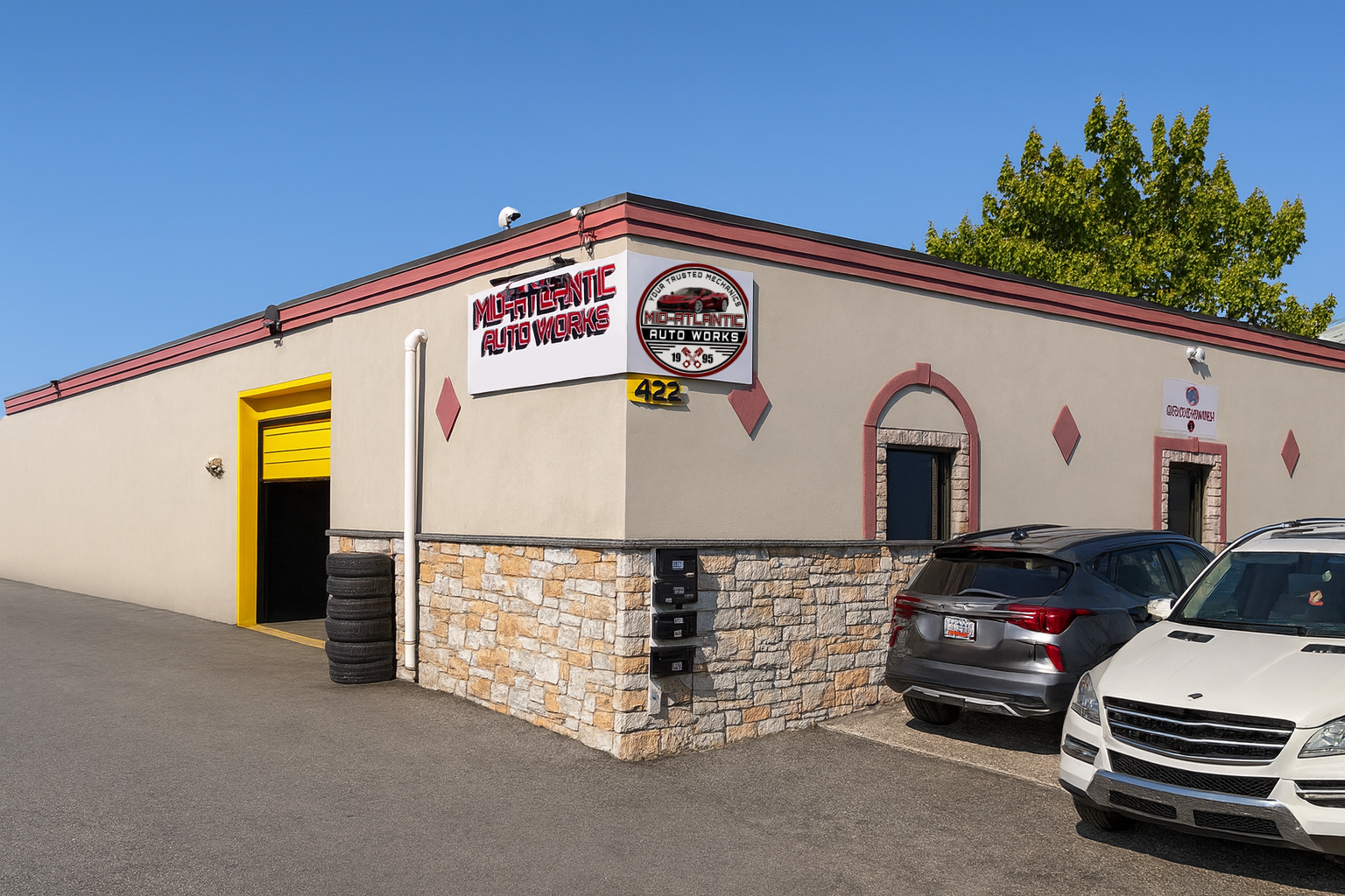 Three people in a garage pose with crossed arms. A car is visible on a lift. All wear black shirts with logos. | Mid Atlantic Autoworks