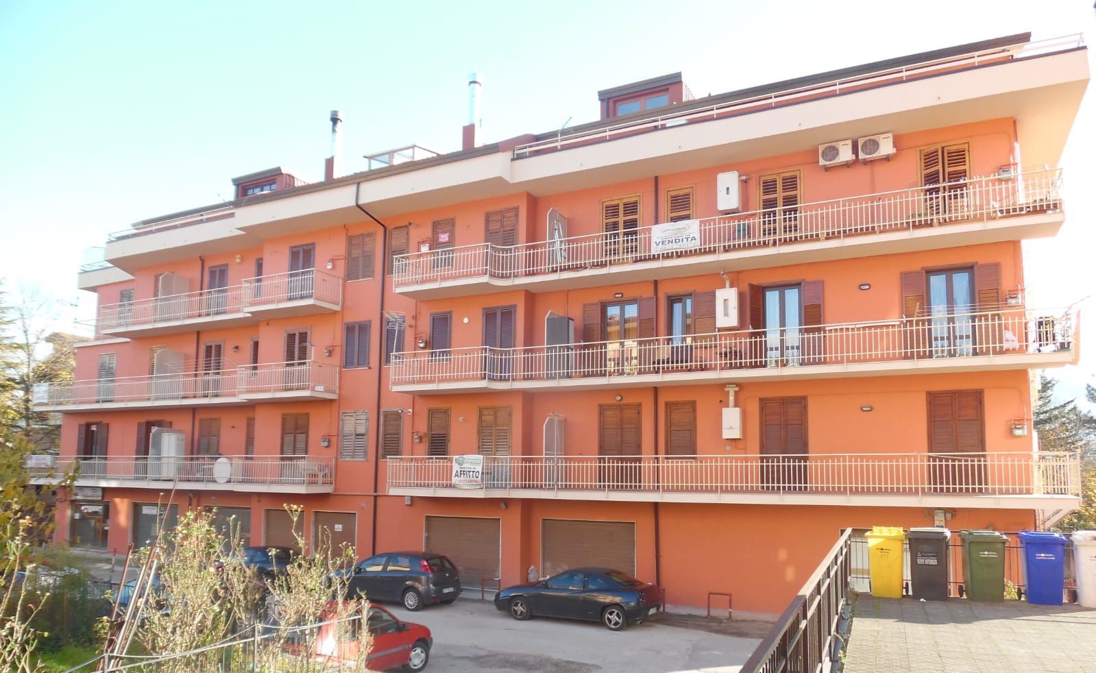 Un grande condominio con molti balconi e macchine parcheggiate davanti.
