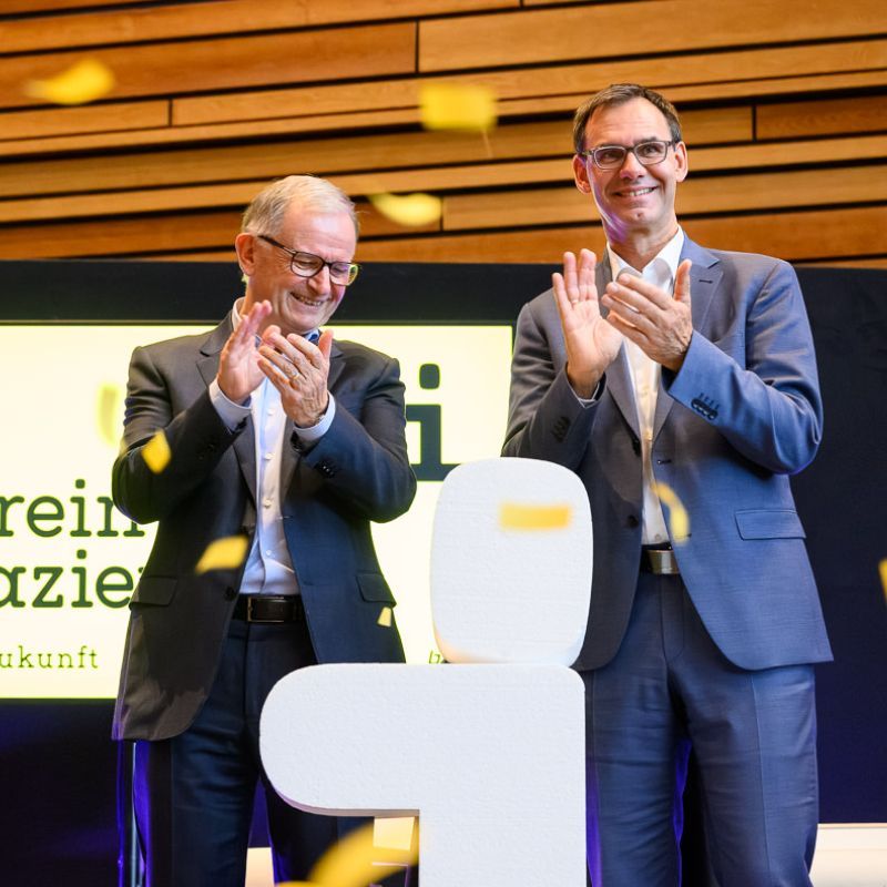 Junge Frau im Laborkittel und mit Schutzbrille lächelt, während sie drinnen an einem wissenschaftlichen Experiment arbeitet.