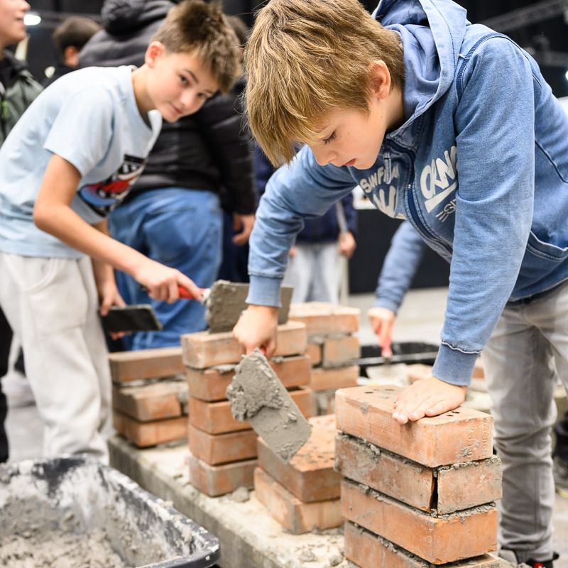 Maurer baut eine Ziegelmauer mit „LYON“ aus Leichtbausteinen. Auf der Mauer sitzen zwei Kuppeln.