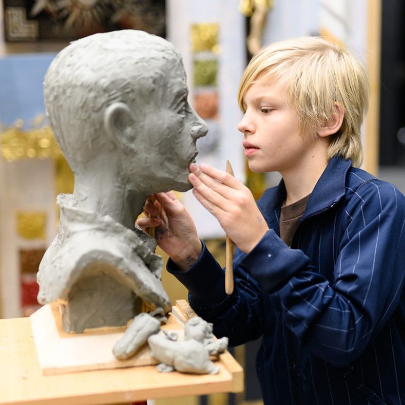 Drei junge Leute bereiten hinter einer Bar einen Drink zu, einer schenkt aus einer Flasche ein.