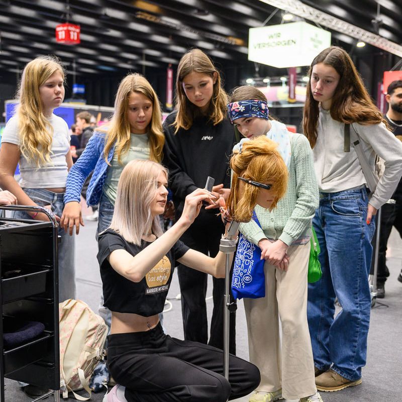 Ein Teenager mit Mütze und Jacke lächelt und steht bei einer Veranstaltung neben einer farbenfrohen Roboterausstellung.