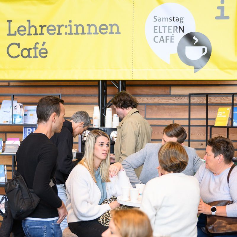 Vier junge Leute füllen bei einer Veranstaltung gelbe Formulare aus, andere im Hintergrund.