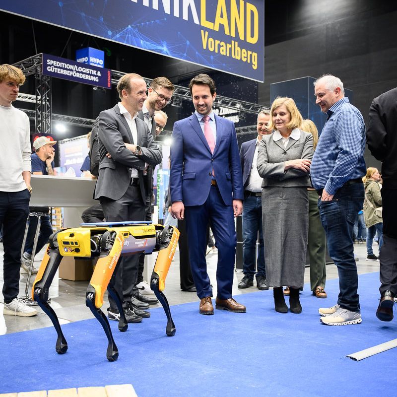Zwei Jungen bauen an einem Tisch in einer Ausstellungshalle einen Roboter. Einer benutzt einen Schraubenzieher.