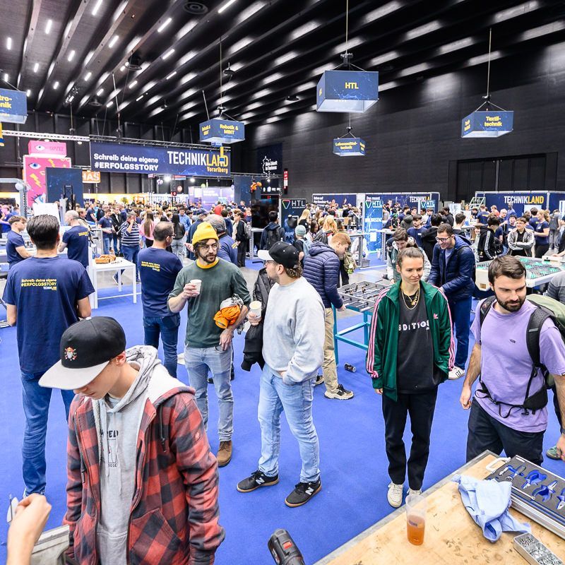 Vier junge Männer schauen bei einer Technikveranstaltung auf einen Laptop.