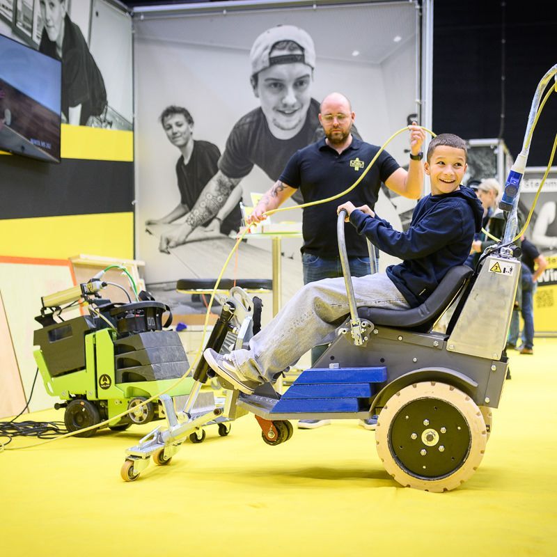Menschen interagieren auf einer Tagung mit einem farbenfrohen Projekttisch, im Hintergrund sind „HAX“-Ballons zu sehen.