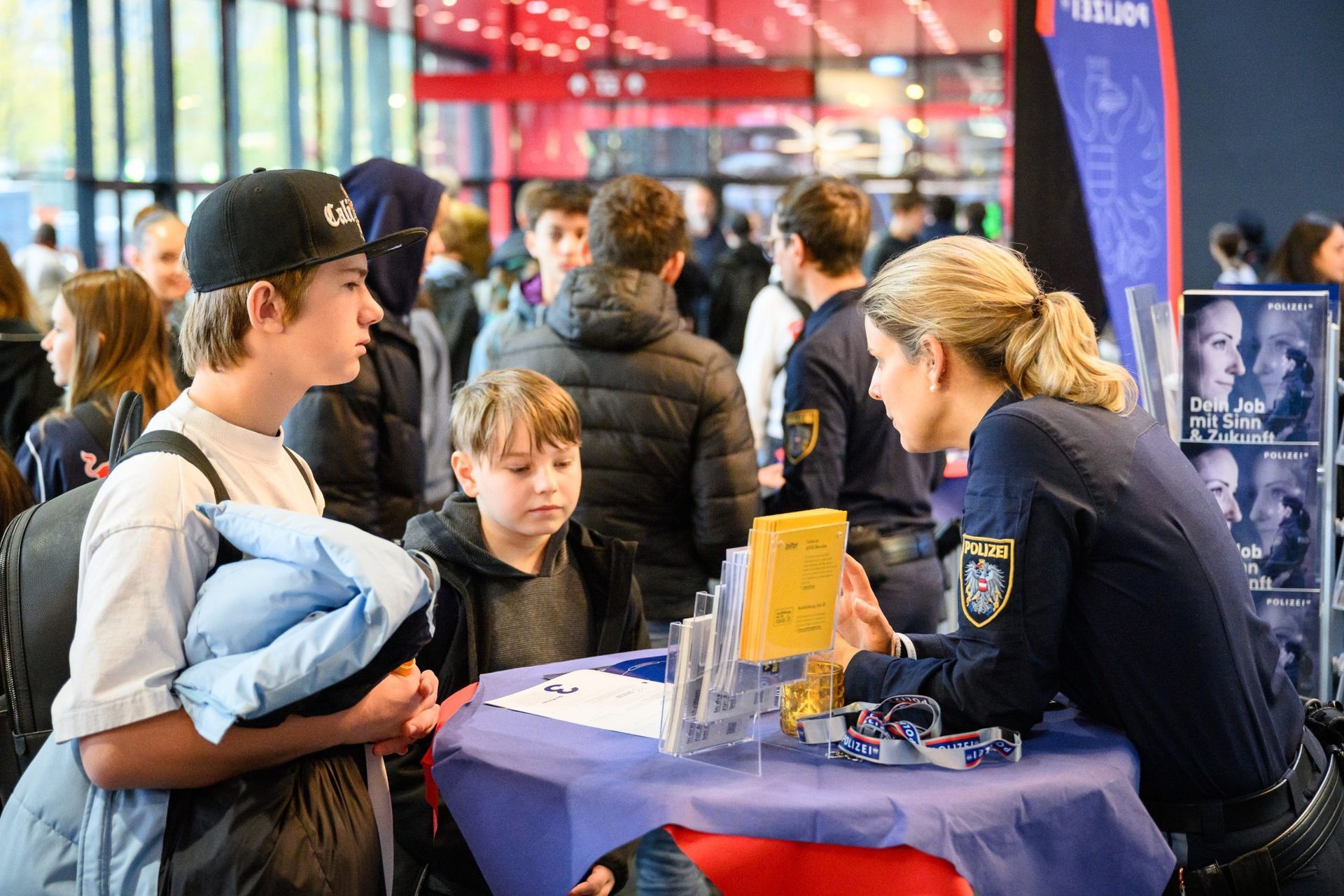 Ein Polizist spricht bei einer Rekrutierungsveranstaltung mit zwei jungen Leuten.