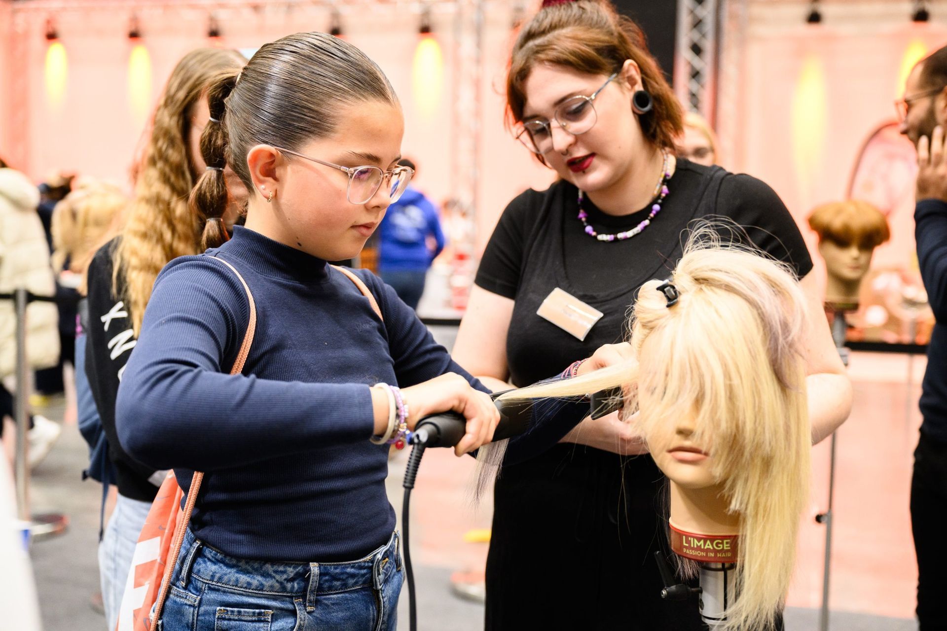Mädchen lernt bei einer Haarshow unter Anleitung eines Lehrers an einer Schaufensterpuppe das Frisieren der Haare.