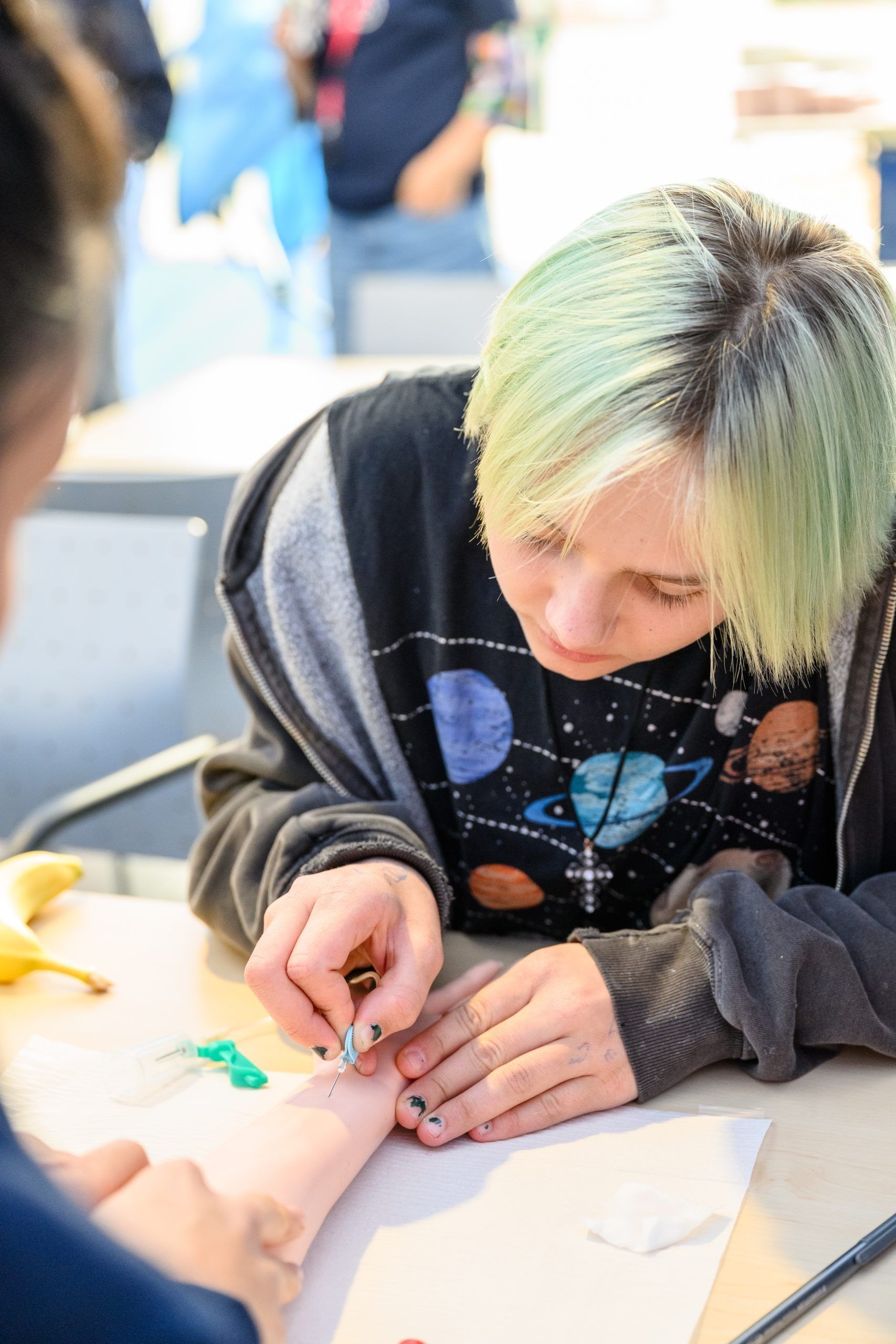 Person mit grün getöntem Haar, die eine Lanzette an einem Fuß verwendet, möglicherweise für eine Blutuntersuchung.