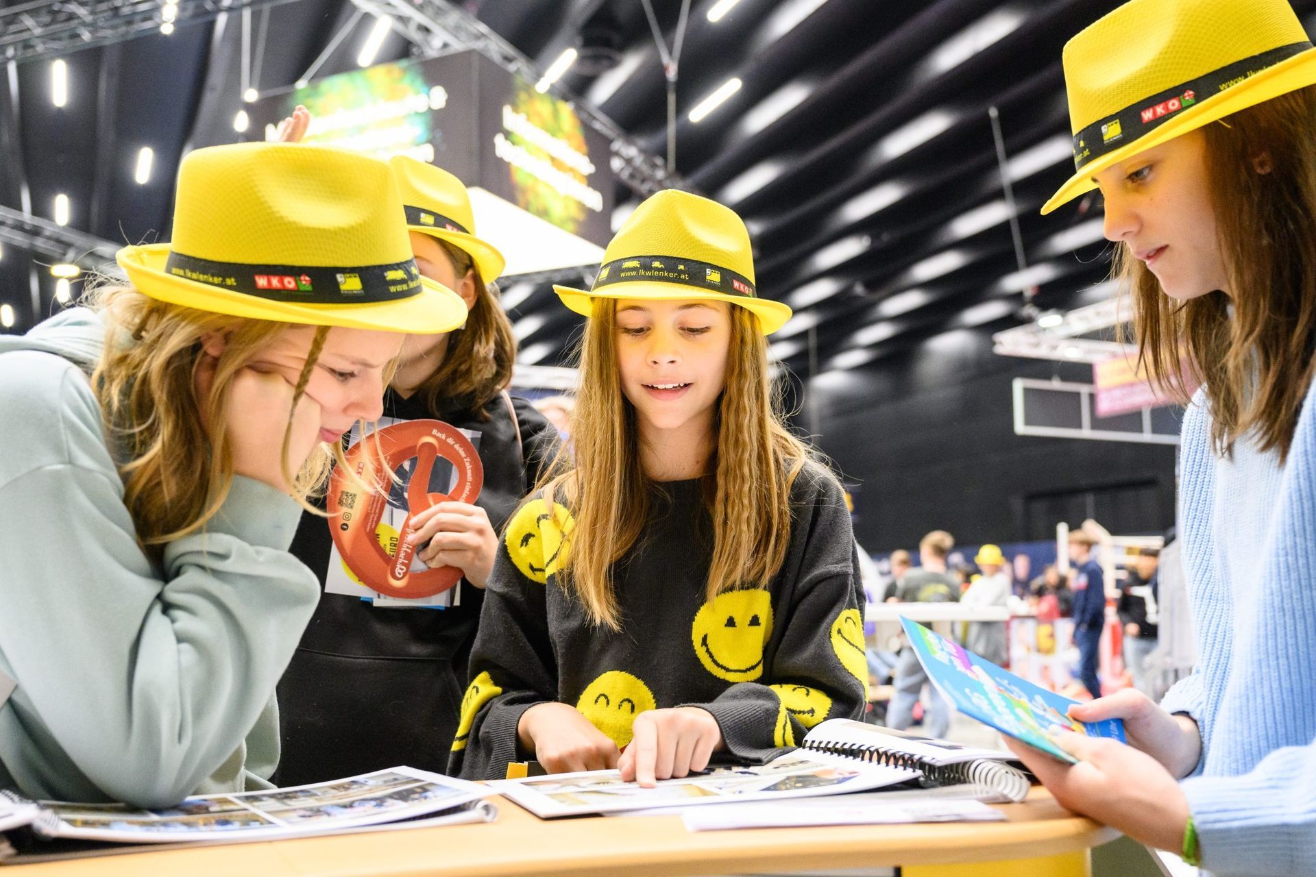 Junge Leute mit gelben Hüten schauen sich an einem Tisch Papiere an.