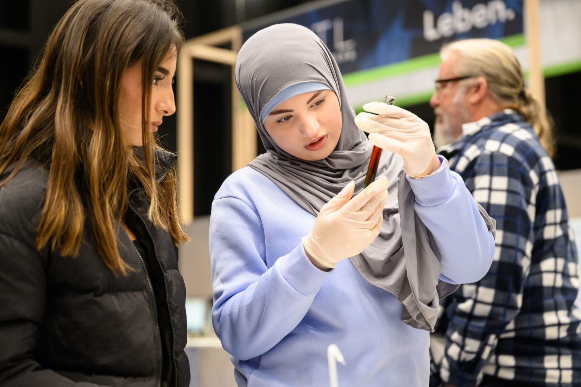 Zwei Frauen und ein Mann untersuchen einen Gegenstand. Eine Frau im Hijab trägt Handschuhe und zeigt darauf.