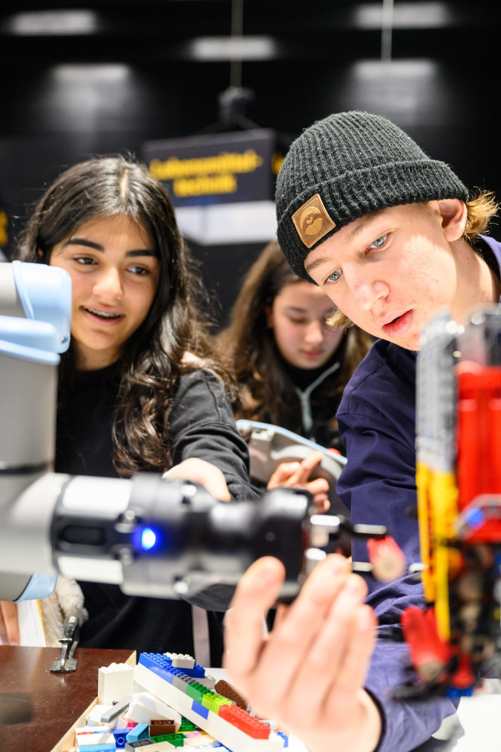 Konzentriert und lächelnd arbeiten zwei Studierende bei einer Robotik-Veranstaltung an einem Roboterarm.